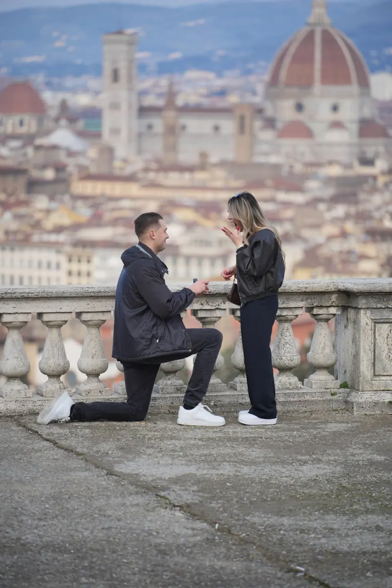 Jordan on one knee proposing to Ysabelle on a stone terrace above Florence, with the Duomo behind them
