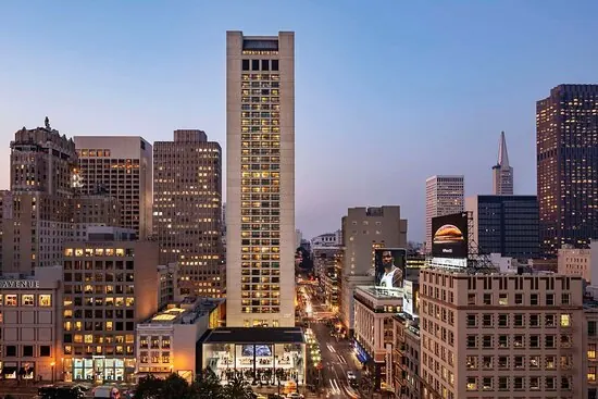 The Grand Hyatt San Francisco tower rising above Union Square at dusk, with the city skyline behind it