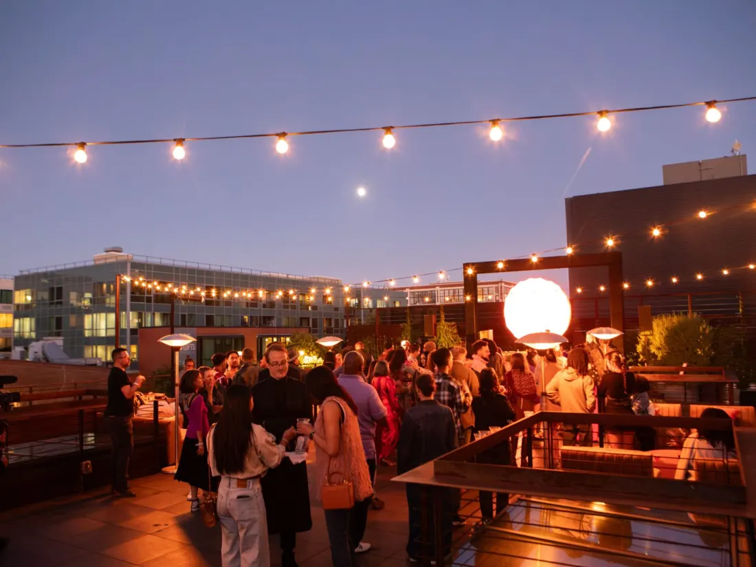 The Pearl's rooftop at dusk, strung with festoon lights and full of guests under a rising moon